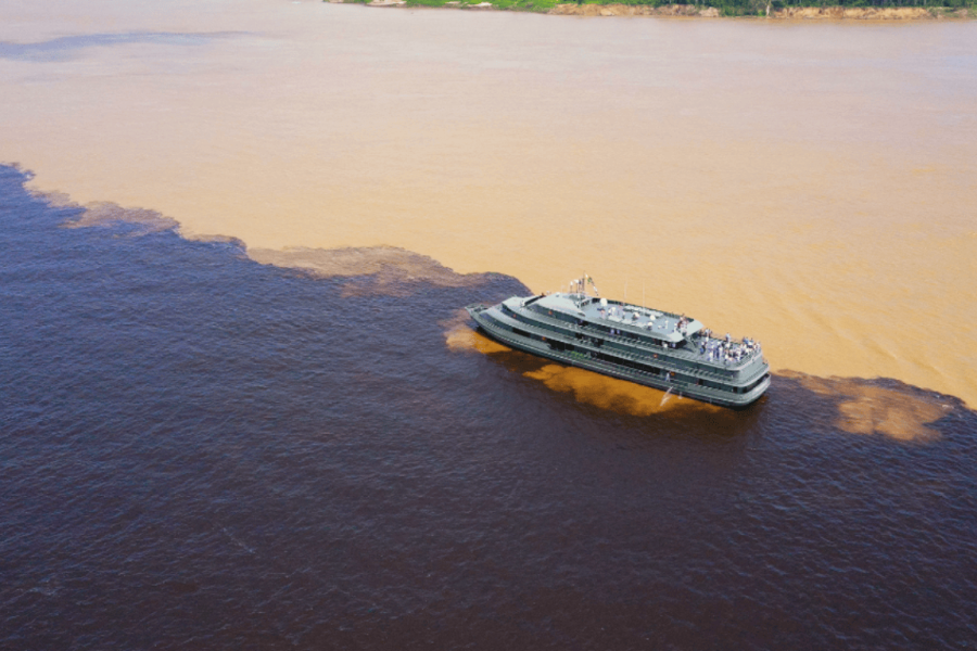 Boat sailing along the Rio Negro in the Amazon, with dark waters contrasting with the meeting of the rivers in the background.