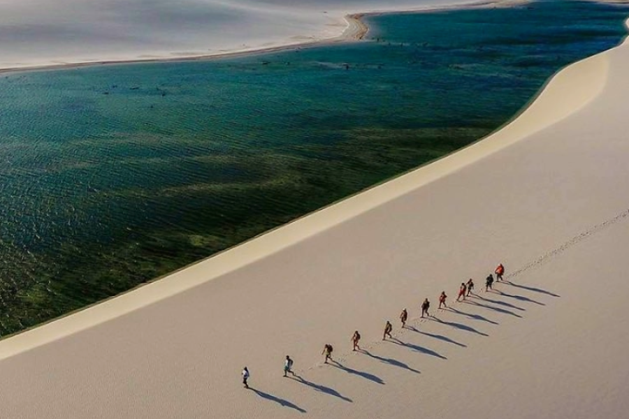Aerial view of the Lençóis Maranhenses dunes with a group walking along the sandy ridge between turquoise-blue lagoons.