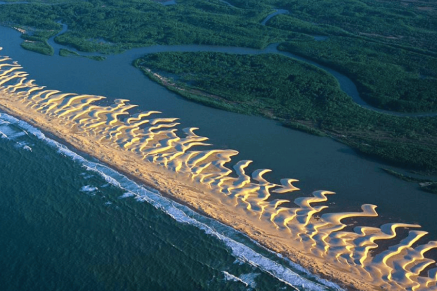 Aerial view of a delta in the Northeast of Brazil, with winding water channels weaving between pale sand dunes and coastal vegetation, creating a truly unique natural landscape.