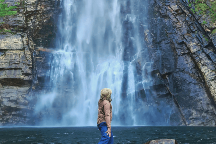 A person admiring a majestic waterfall in the Serra da Canastra, surrounded by towering rock cliffs and native vegetation from Minas Gerais.