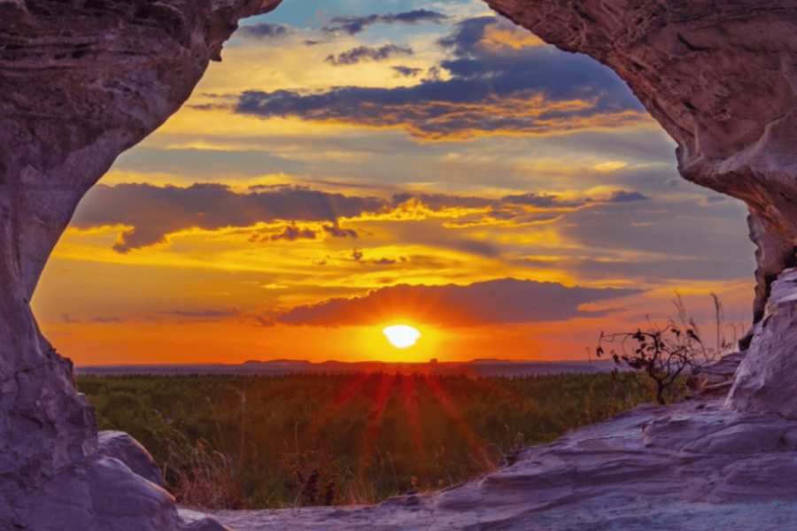 Sunset seen through the Sun Arch in Jalapão, with the sun shining on the horizon and rocks framing the natural landscape.