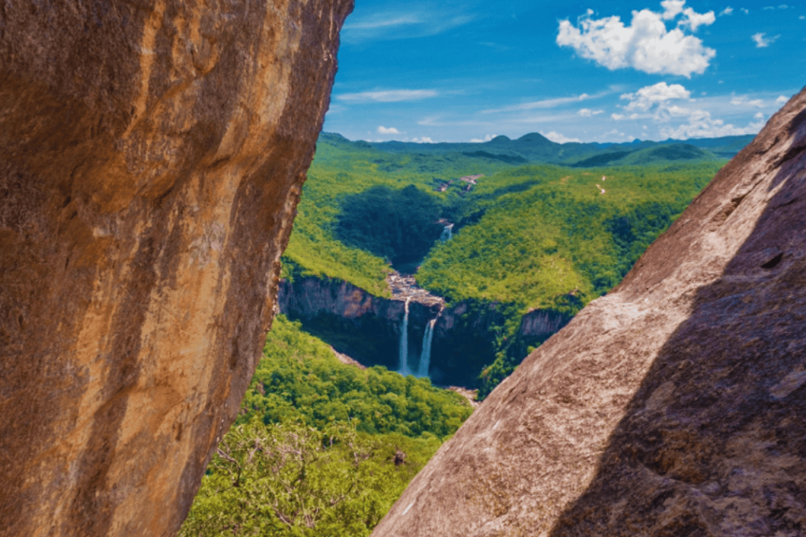View of the waterfall from the Janela Lookout, surrounded by rock formations and cerrado vegetation in Chapada dos Veadeiros, Goiás.