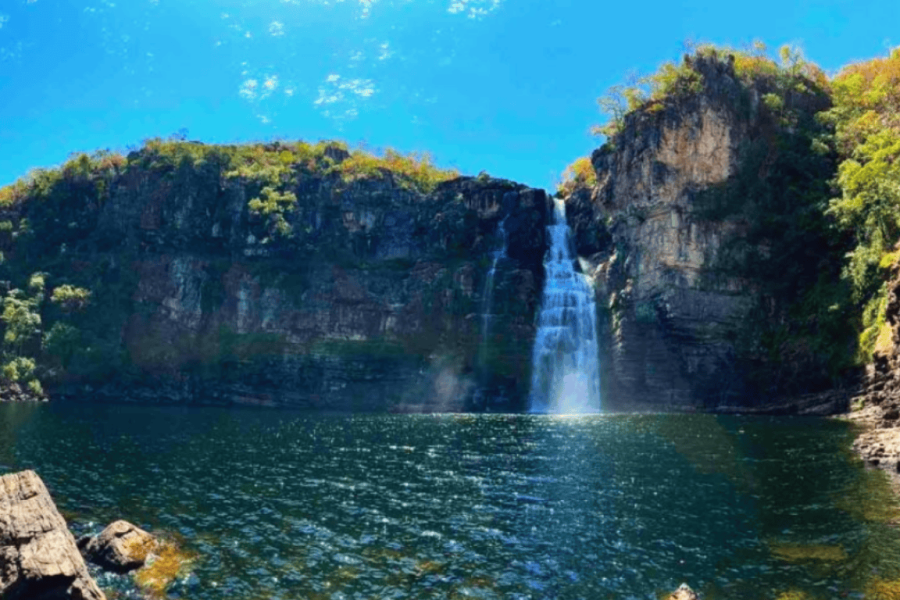 View of Garimpão Waterfall in Chapada dos Veadeiros, where an impressive cascade plunges between rocky cliffs into a dark, deep pool, surrounded by the characteristic savanna vegetation of the cerrado.