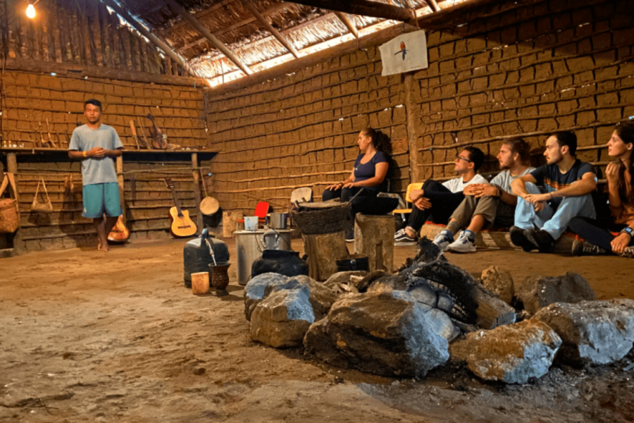 A Guarani Mbya person seated in a traditional house of the Tenondé Porã village, taking part in a cultural discussion circle within an indigenous community space.