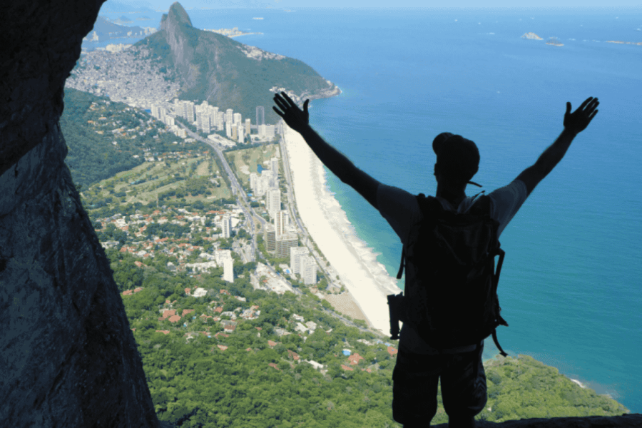 Person standing at the Garganta do Céu viewpoint, on Pedra da Gávea, arms outstretched, enjoying a panoramic view of the beaches and the city of Rio de Janeiro.