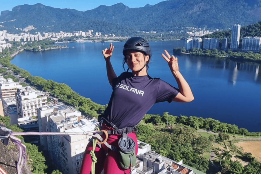 Person smiling while climbing at Praia Vermelha in Rio de Janeiro, with a panoramic view of Lagoa Rodrigo de Freitas and the city in the background.
