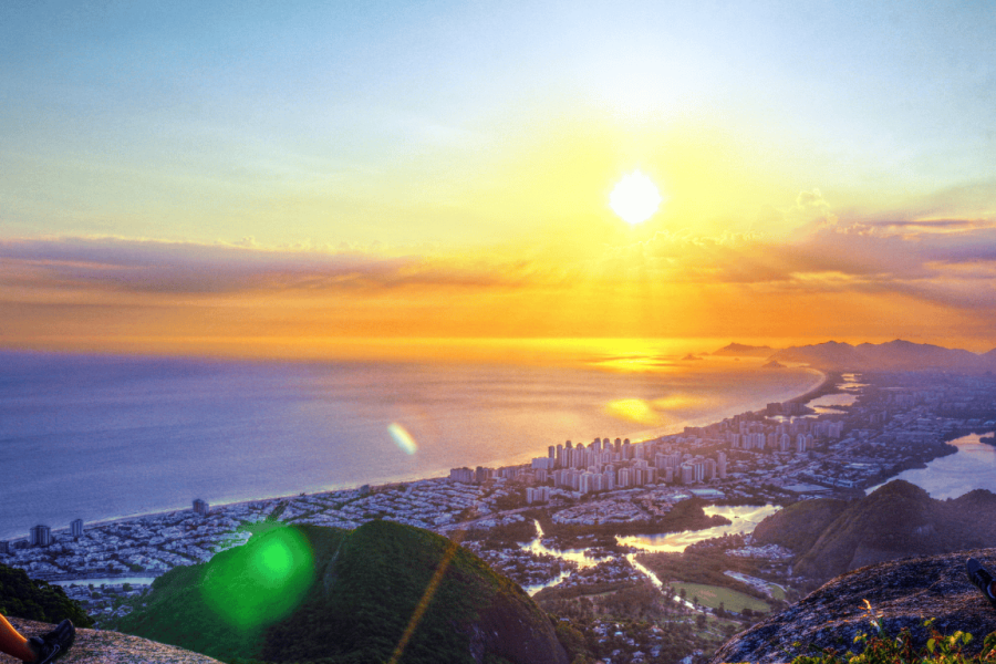 Panoramic view of the sunset from Pedra Bonita in Rio de Janeiro, with the sea, the city, and mountains in the background, all bathed in golden light.