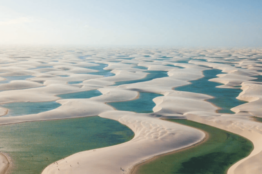 Aerial view of the Lençóis Maranhenses with white sand dunes interspersed with green and blue lagoons amid Maranhão’s natural landscape.